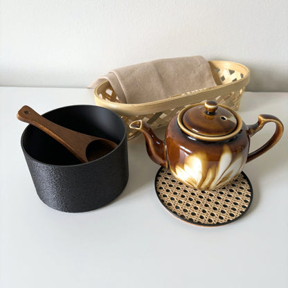 Black COZI minimalist canister on a kitchen counter, holding a teapot and cup on its rattan lid by Sonnihaus