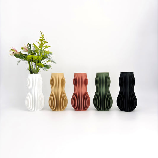 A collection of five 3D-printed HOLI vases in various colors including white, beige, brown, green, and black, displayed in a row with a white flower in the background.