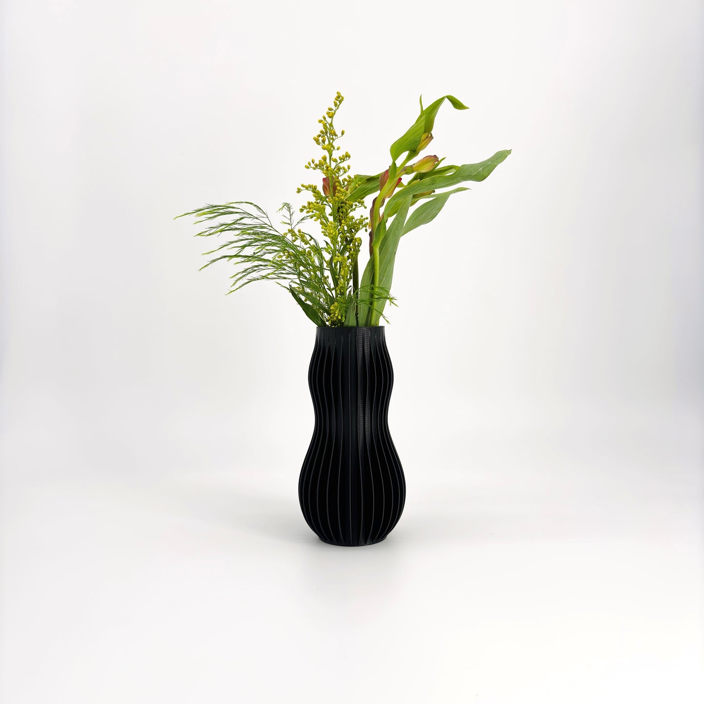 A collection of five 3D-printed HOLI vases in various colors including white, beige, brown, green, and black, displayed in a row with a white flower in the background.