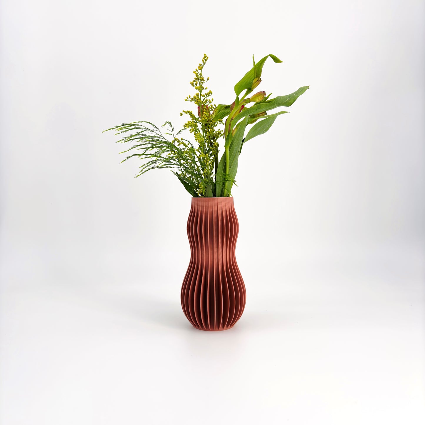 A collection of five 3D-printed HOLI vases in various colors including white, beige, brown, green, and black, displayed in a row with a white flower in the background.
