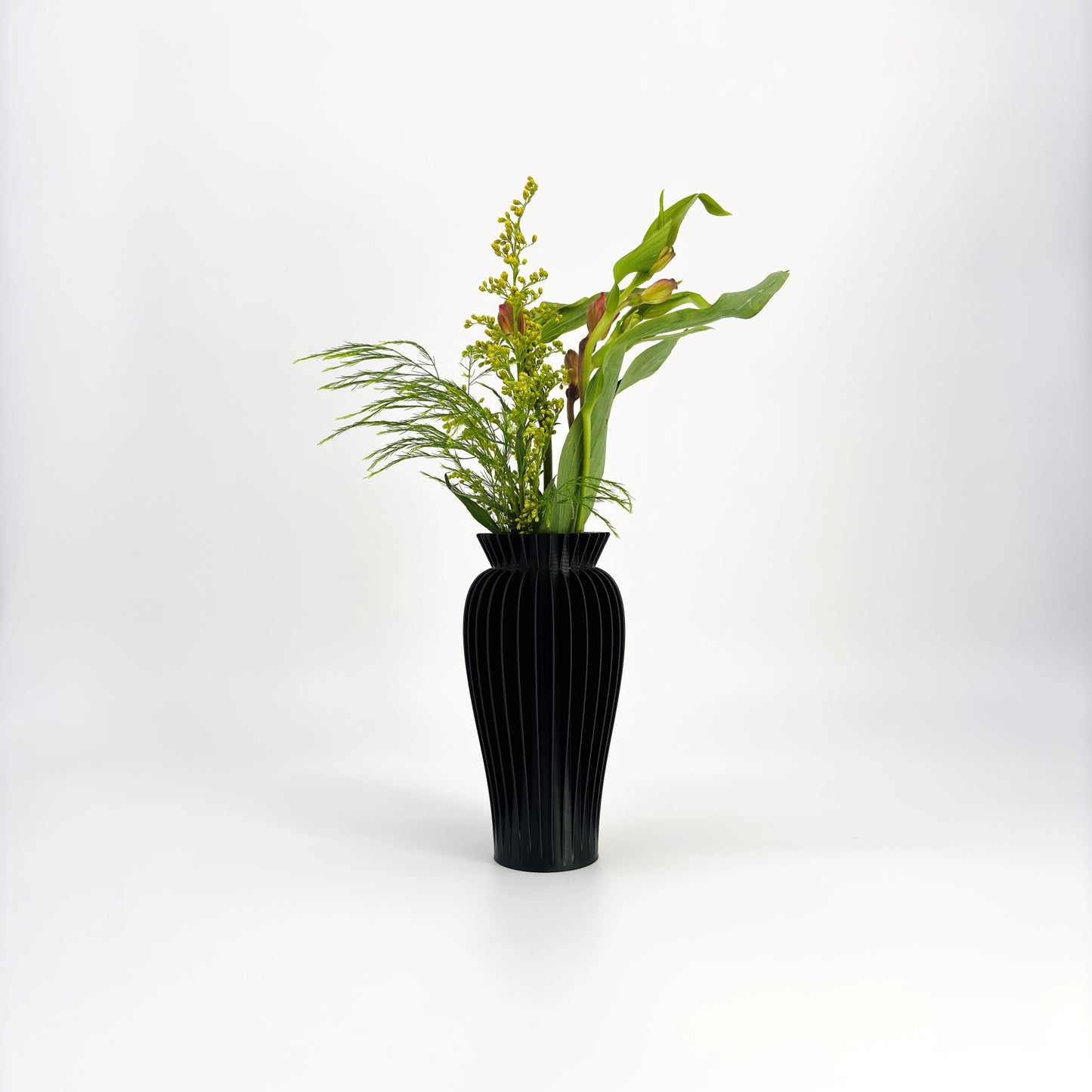 A collection of five MAE Vases in various colors including white, pink, beige, green, and black, displayed against a white background with a floral arrangement in the background.