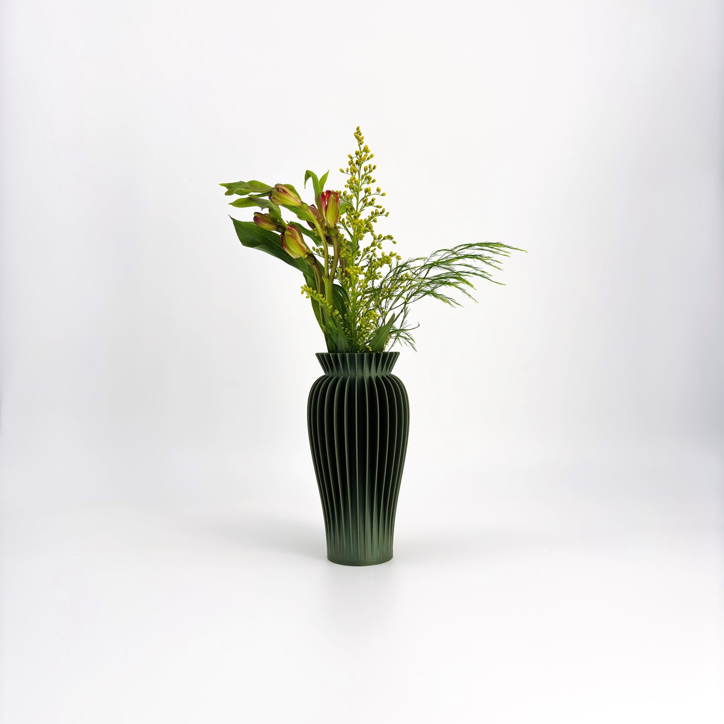 A collection of five MAE Vases in various colors including white, pink, beige, green, and black, displayed against a white background with a floral arrangement in the background.
