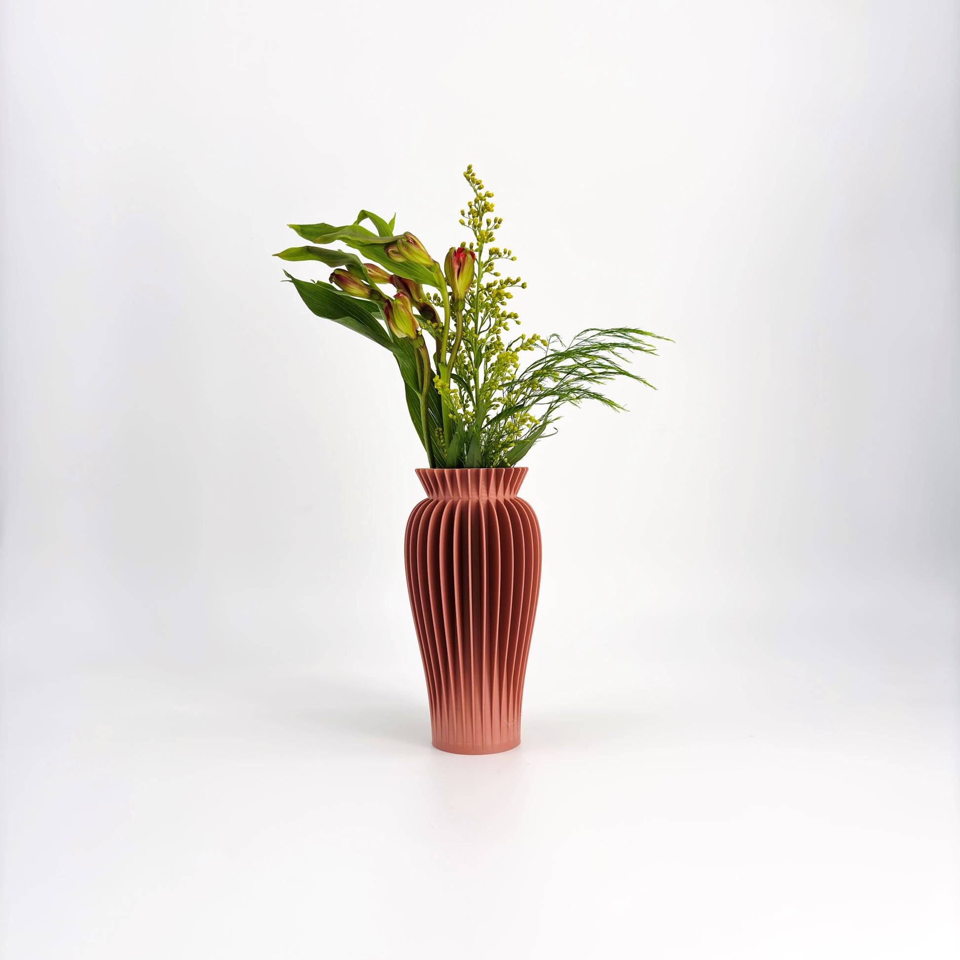 A collection of five MAE Vases in various colors including white, pink, beige, green, and black, displayed against a white background with a floral arrangement in the background.