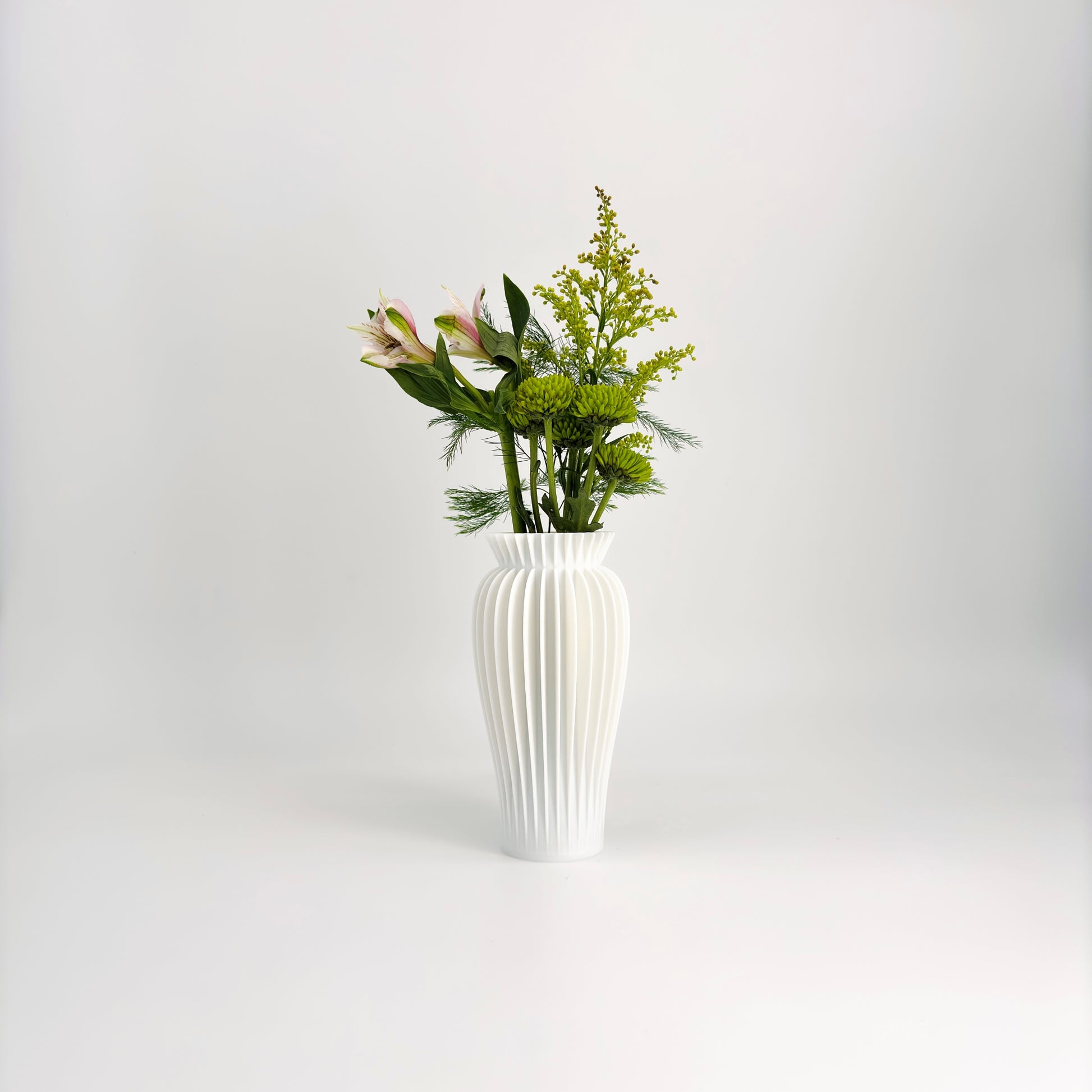 A collection of five MAE Vases in various colors including white, pink, beige, green, and black, displayed against a white background with a floral arrangement in the background.